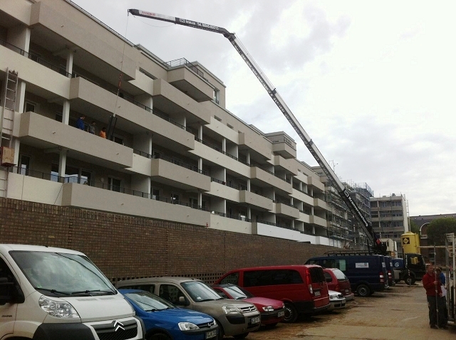 Bild großes Gebäude im Rohbau. ein Kran hat  ein Arbeitsgerät in den Seilen hängen.